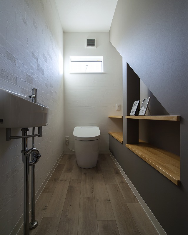 階段下の空間を活かしたトイレは、こだわりの棚で収納力とデザイン性を両立。
落ち着いた色味とアクセントクロスが、コンパクトながらも洗練された印象を与えます。
小窓から自然光が入り、明るく快適な空間に仕上がっています。
