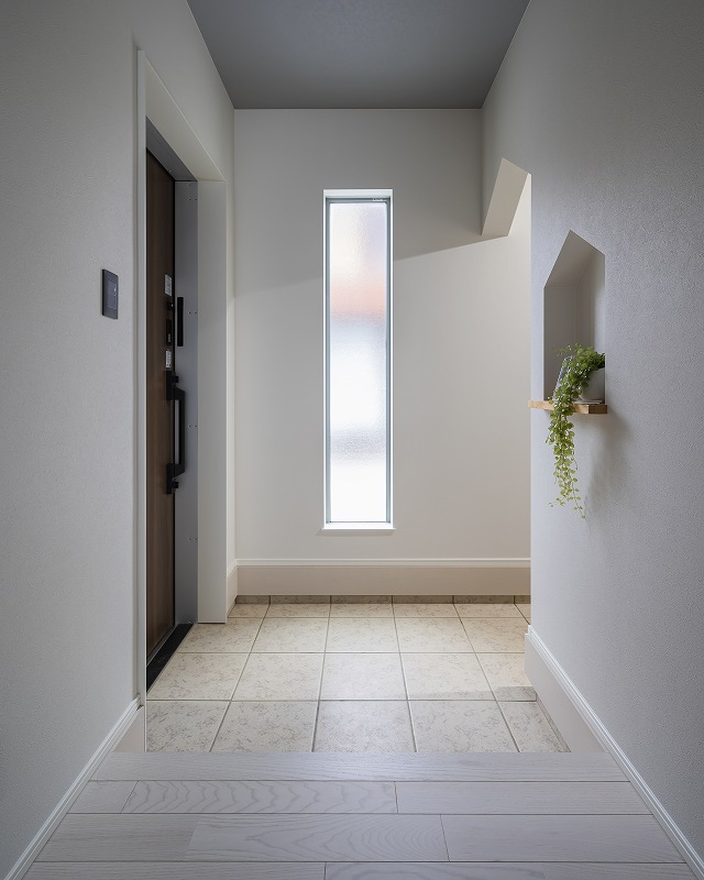 縦長の窓からやわらかな自然光が差し込む、明るく開放的な玄関。
木目調の玄関ドアが空間にナチュラルなアクセントを加え、訪れる人をやさしく迎え入れます。