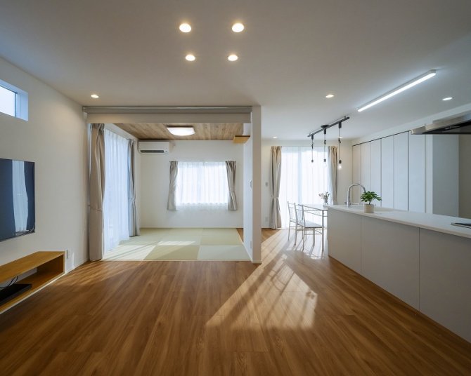 窓から差し込む自然光が明るく開放的なLDK。リビングのフローリングと畳スペースが調和し、洋と和の魅力を併せ持つ居心地の良い設計。白を基調としたシンプルながらも上質な雰囲気を添え、実用性とデザイン性を兼ね備えた住空間です。